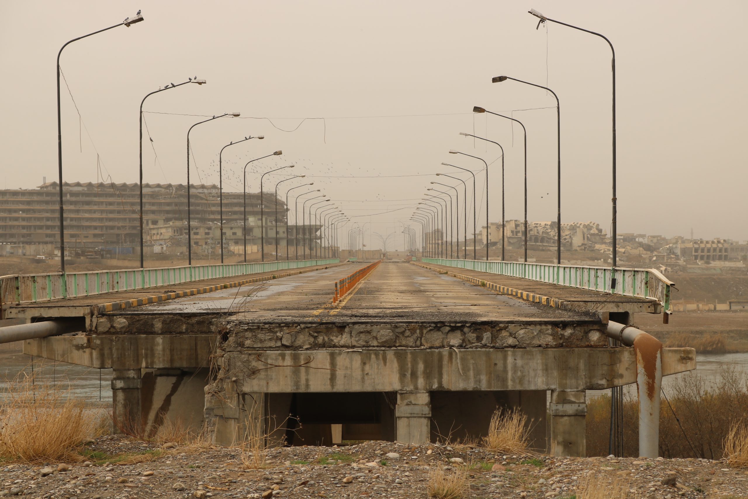 An empty two lane bridge, with one broken end, lined by streetlamps