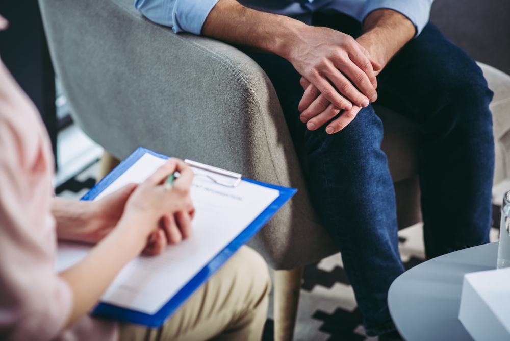 Cropped shot of female psychologist listening to male patient and making notes in document on clipboard